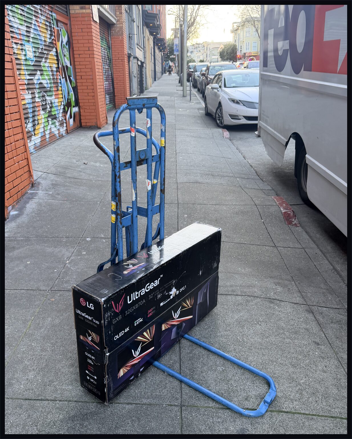 LG UltraGear monitor box on a hand truck on the sidewalk